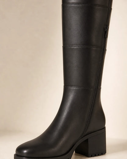 Black chunky knee-high boot showing the panel seams, side zip, lug sole and block heel.