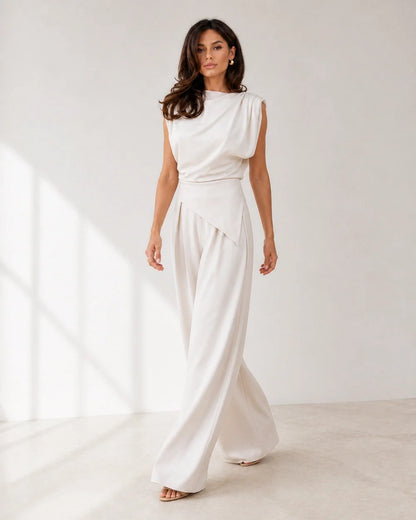 Women's white asymmetric draped top and wide-leg trousers set, walking view.